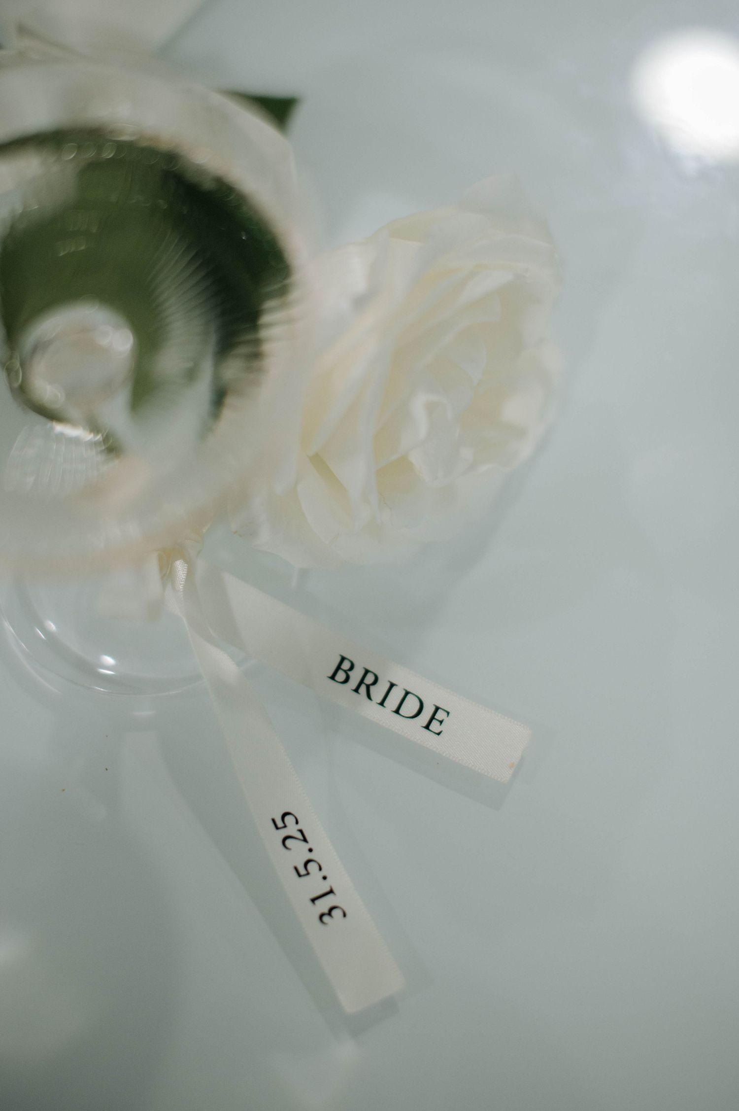 Small white place card marked 'BRIDE' sits beside a delicate white ribbon at a wedding table setting.