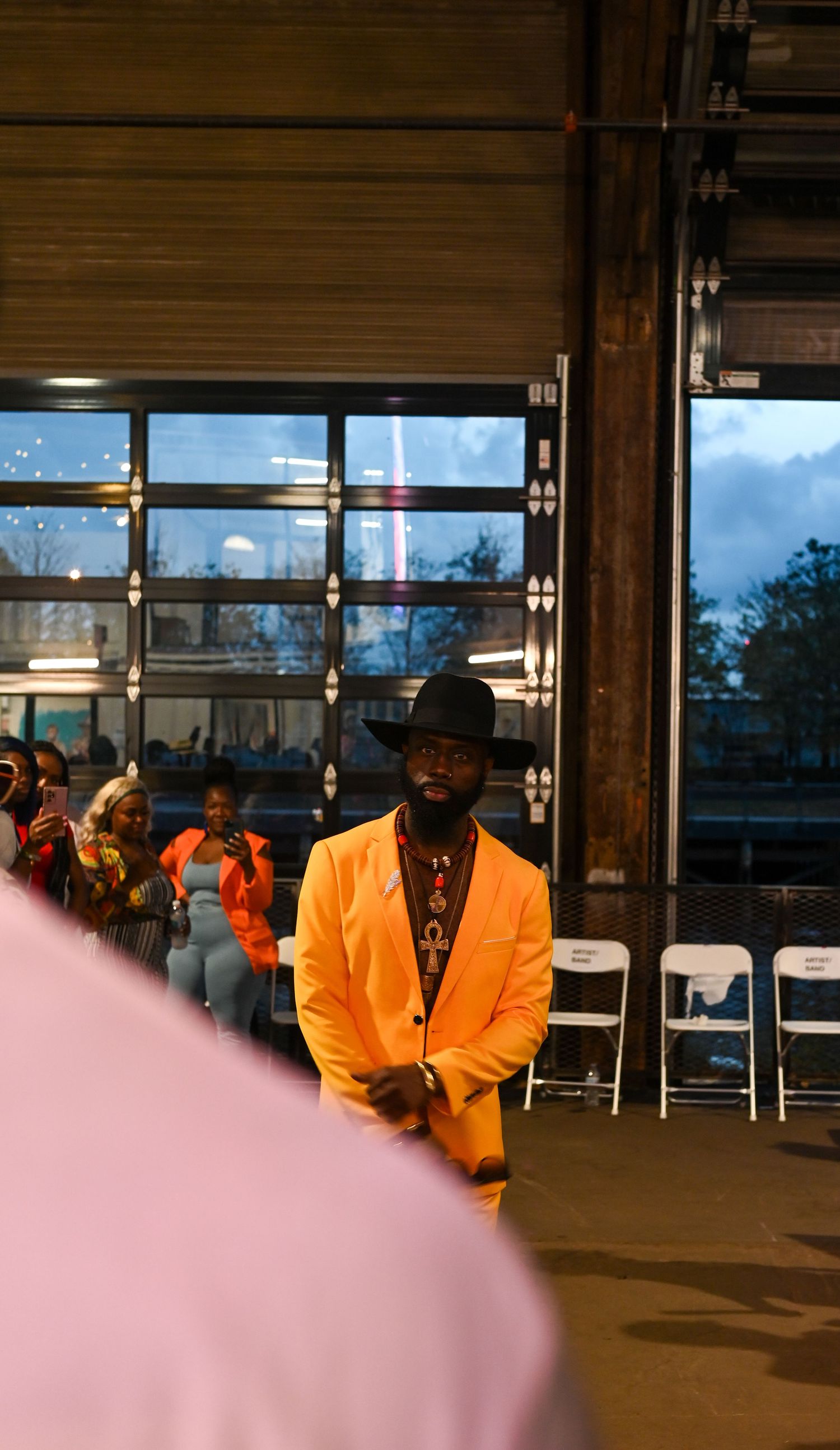 People wearing bright orange blazers stand in silhouette against large windows in an illuminated indoor space.