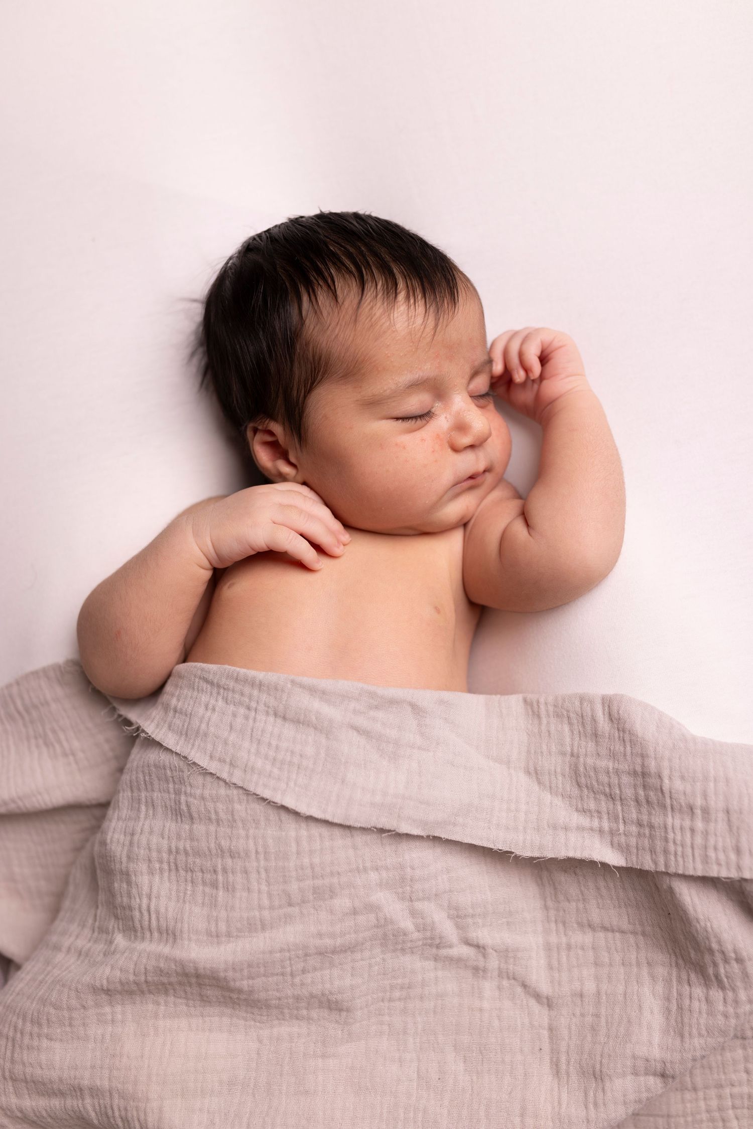 Baby wearing pink headband sits in white wooden barrel prop with peach roses for newborn photography session.