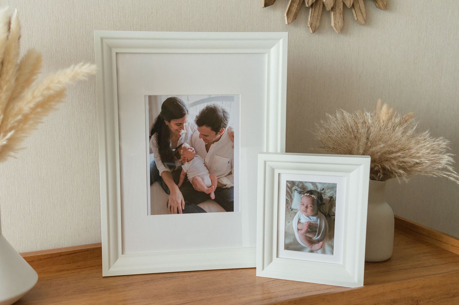 White framed photos displayed on a white shelf with pampas grass and boho decor elements create an elegant gallery wall.