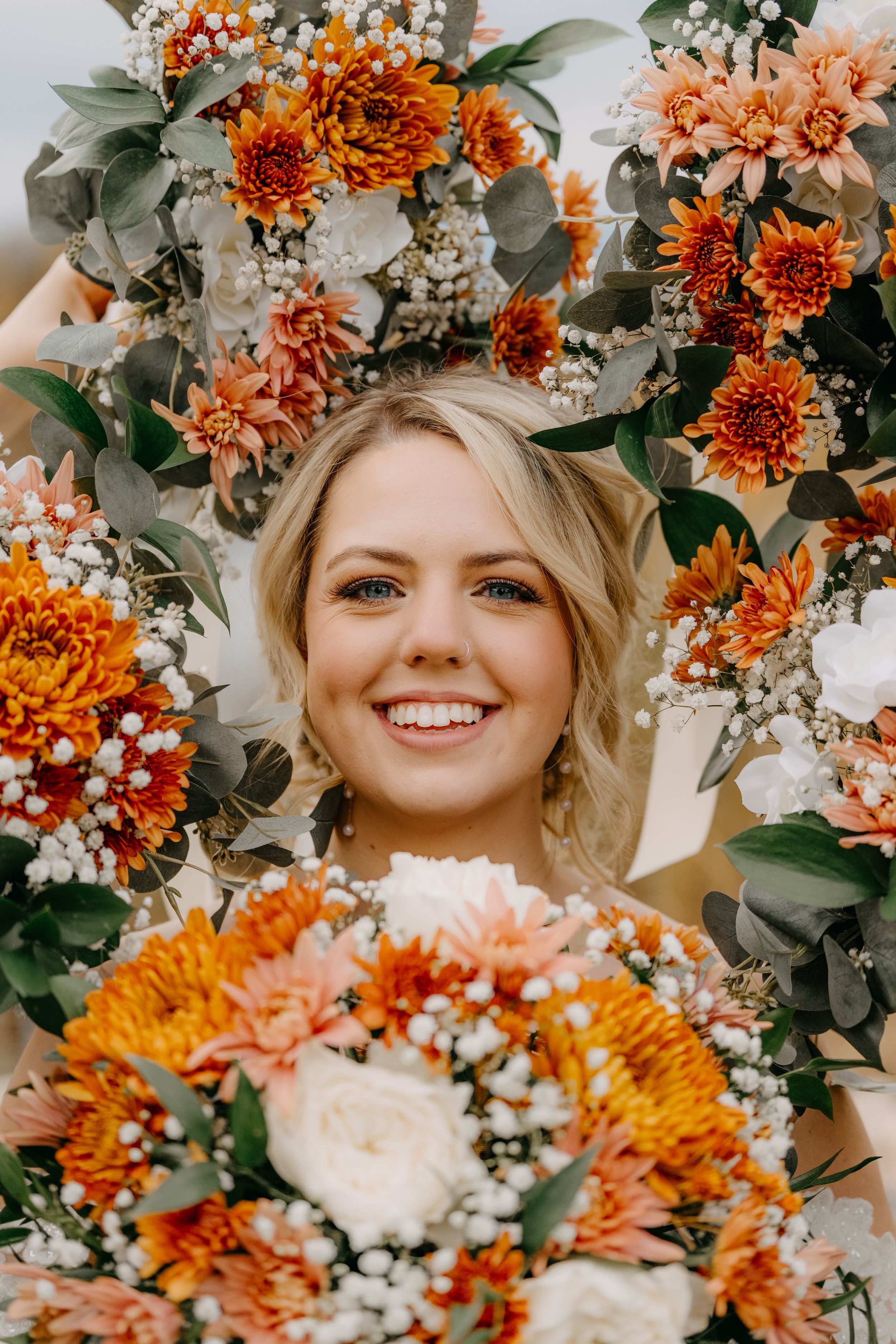 Floral portrait surrounded by vibrant orange chrysanthemums, peach dahlias, white baby's breath and eucalyptus leaves.