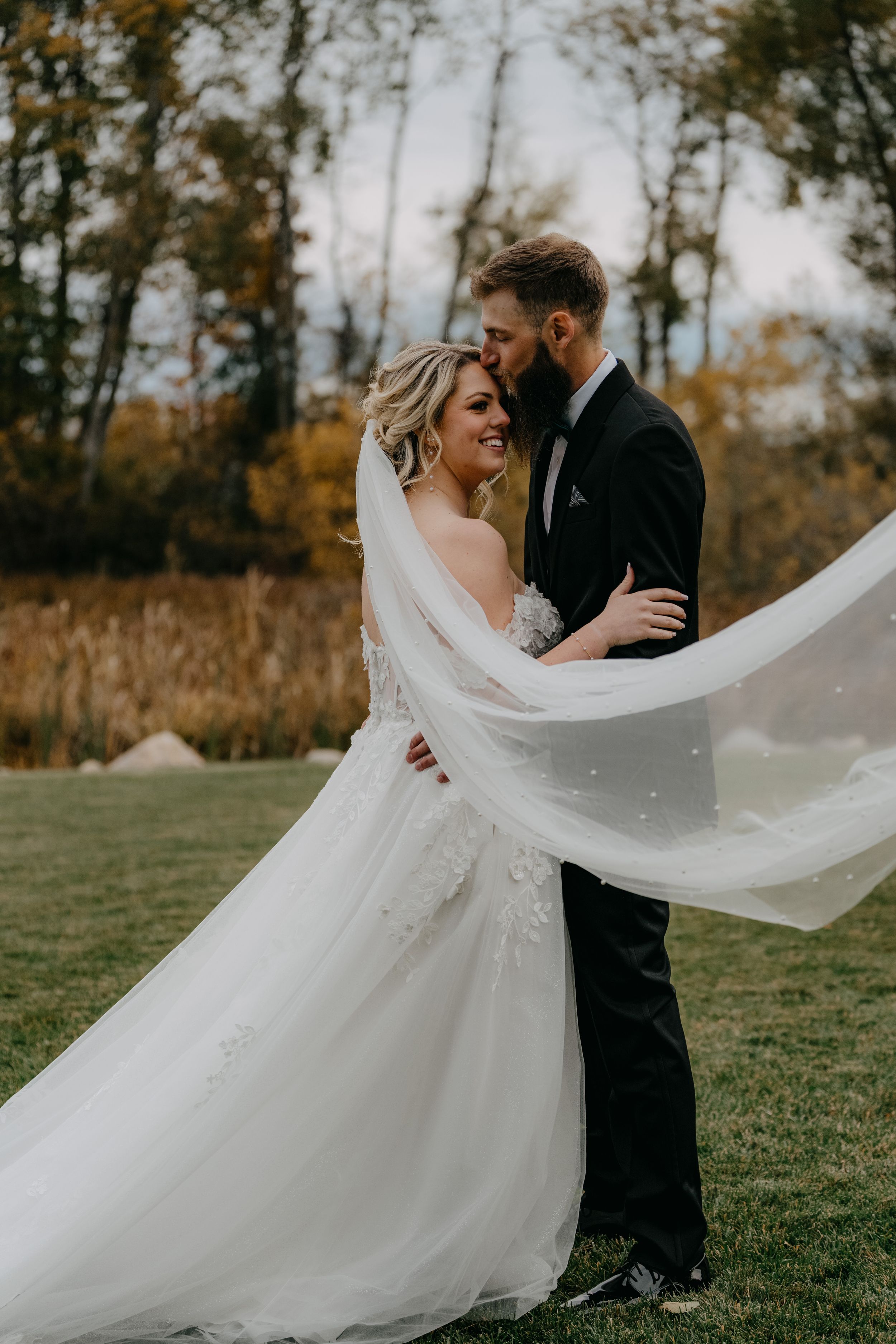 Romantic wedding couple embraces outdoors with bride's flowing white veil catching the autumn breeze in series of photos.