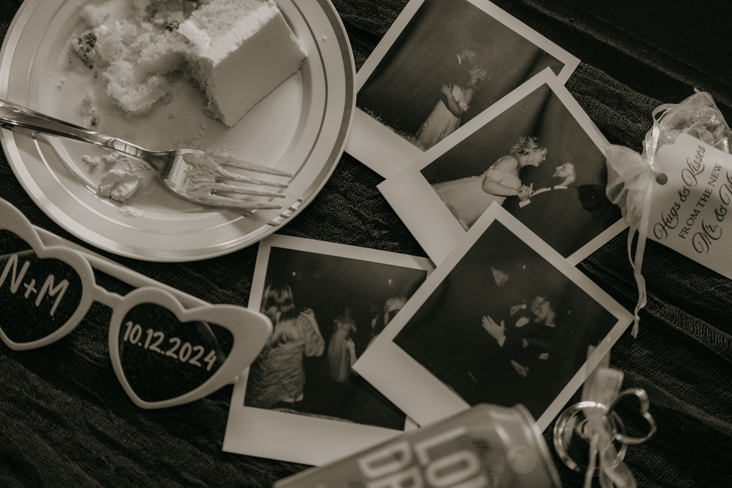 Black and white photo of instant polaroid photographs scattered on a dark wooden surface with a plate and heart decoration.
