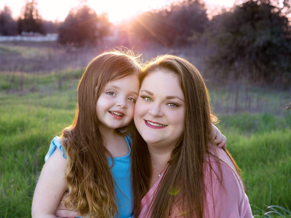 Two people in pink and blue pose together outdoors in a grassy field during golden hour sunset lighting.