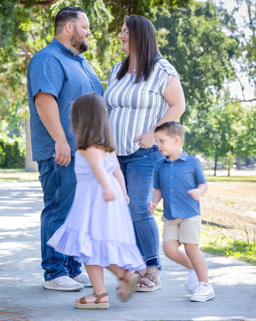 Family enjoying a playful moment together on a sunny path with trees in the background.
