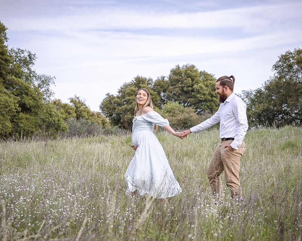 A couple dances together in a wildflower meadow, with her white dress flowing as they spin on a cloudy summer day.