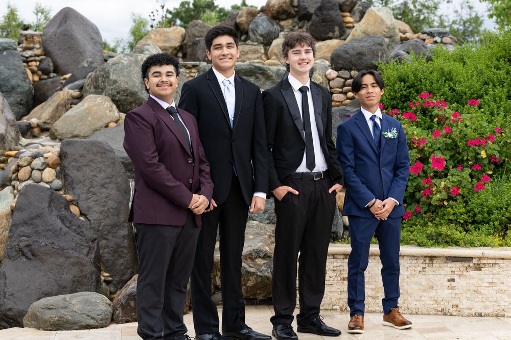 Four teenage boys in formal suits pose together outdoors near rocks for a special occasion.