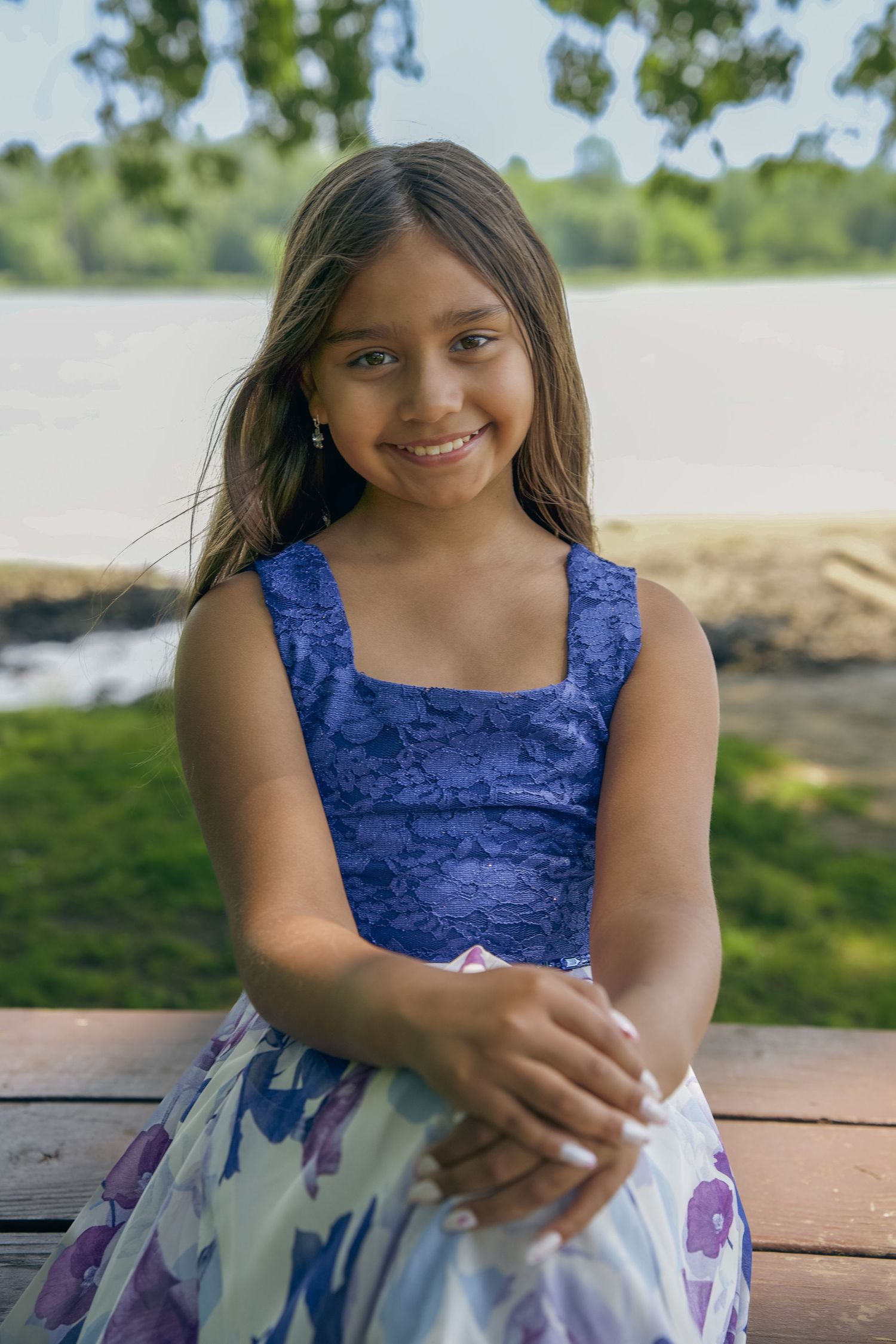 A young person in a blue velvet top and floral skirt sits outdoors on a sunny day.