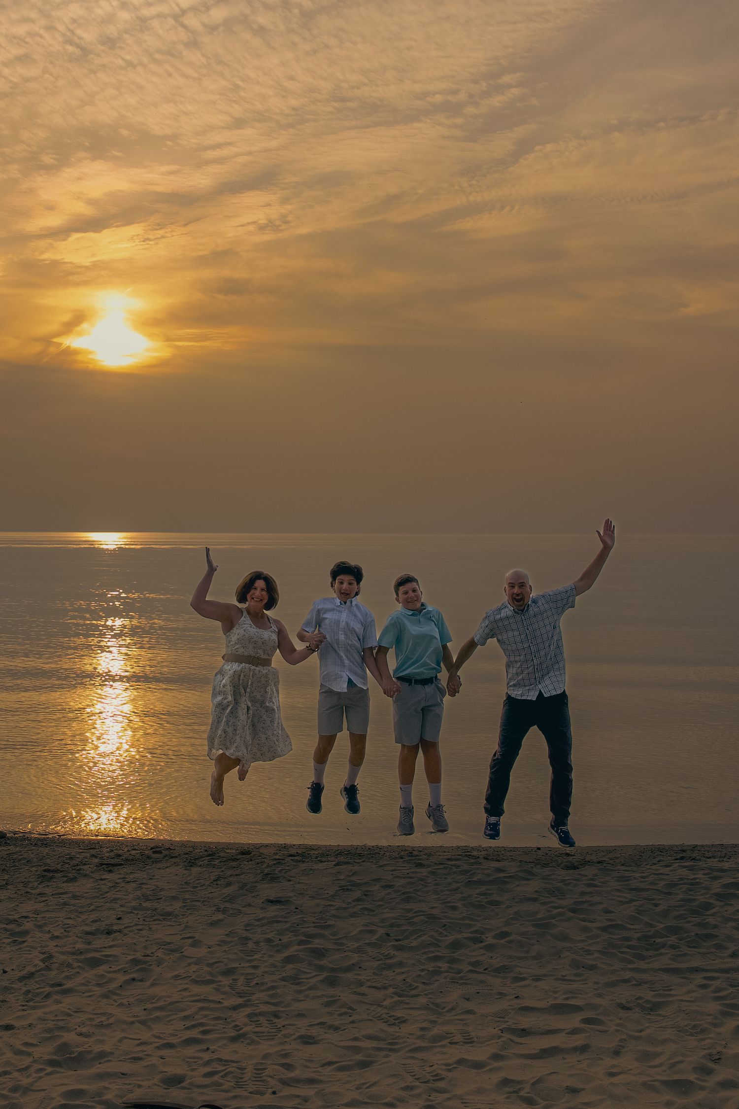 Four people jumping joyfully on a beach at sunset with golden light reflecting on the ocean waters.