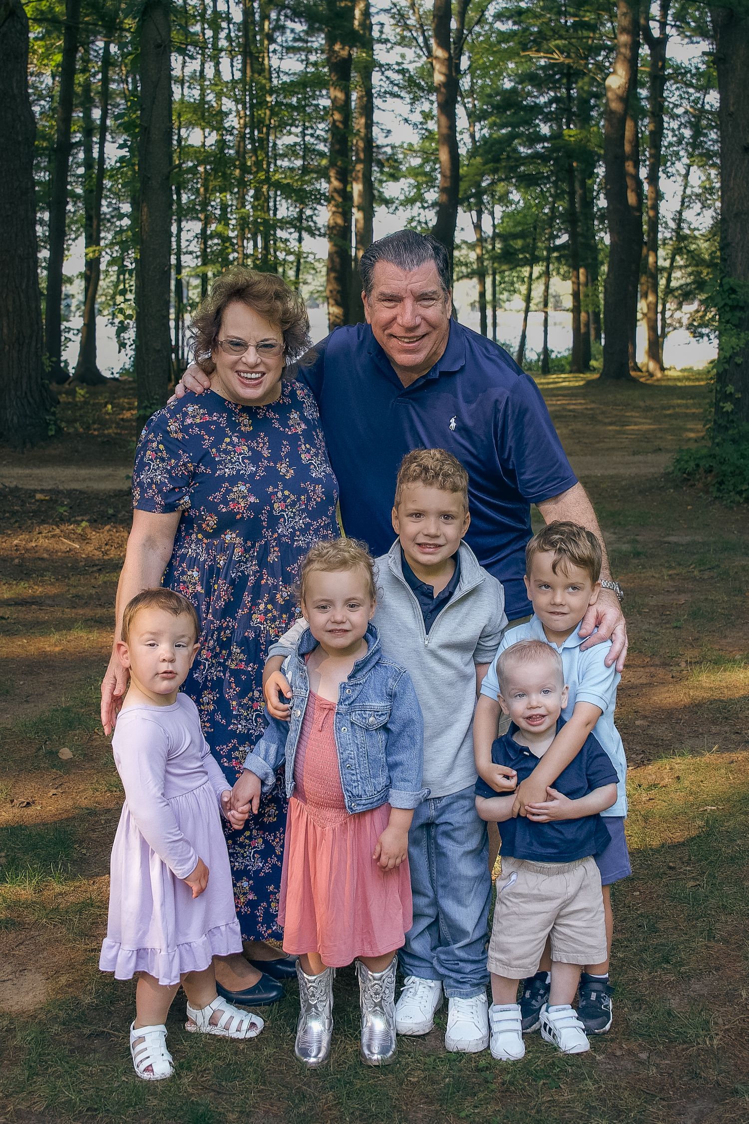 A family poses together in a wooded outdoor setting during a casual photo session.