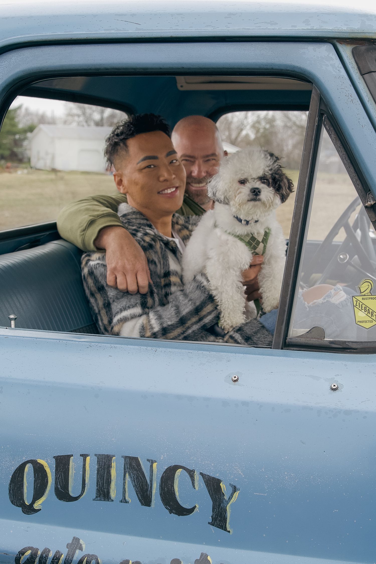 A small white dog sits in a light blue vehicle with "Quincy" written on the side.