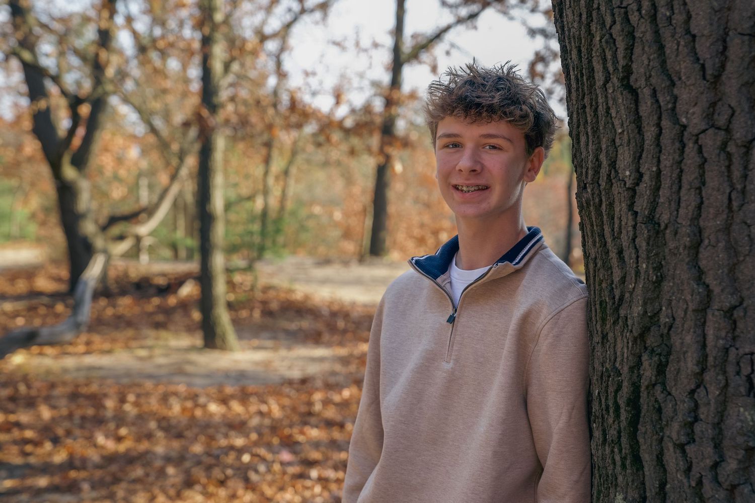Person wearing a sleeveless gray shirt poses in a wooded outdoor setting during autumn.
