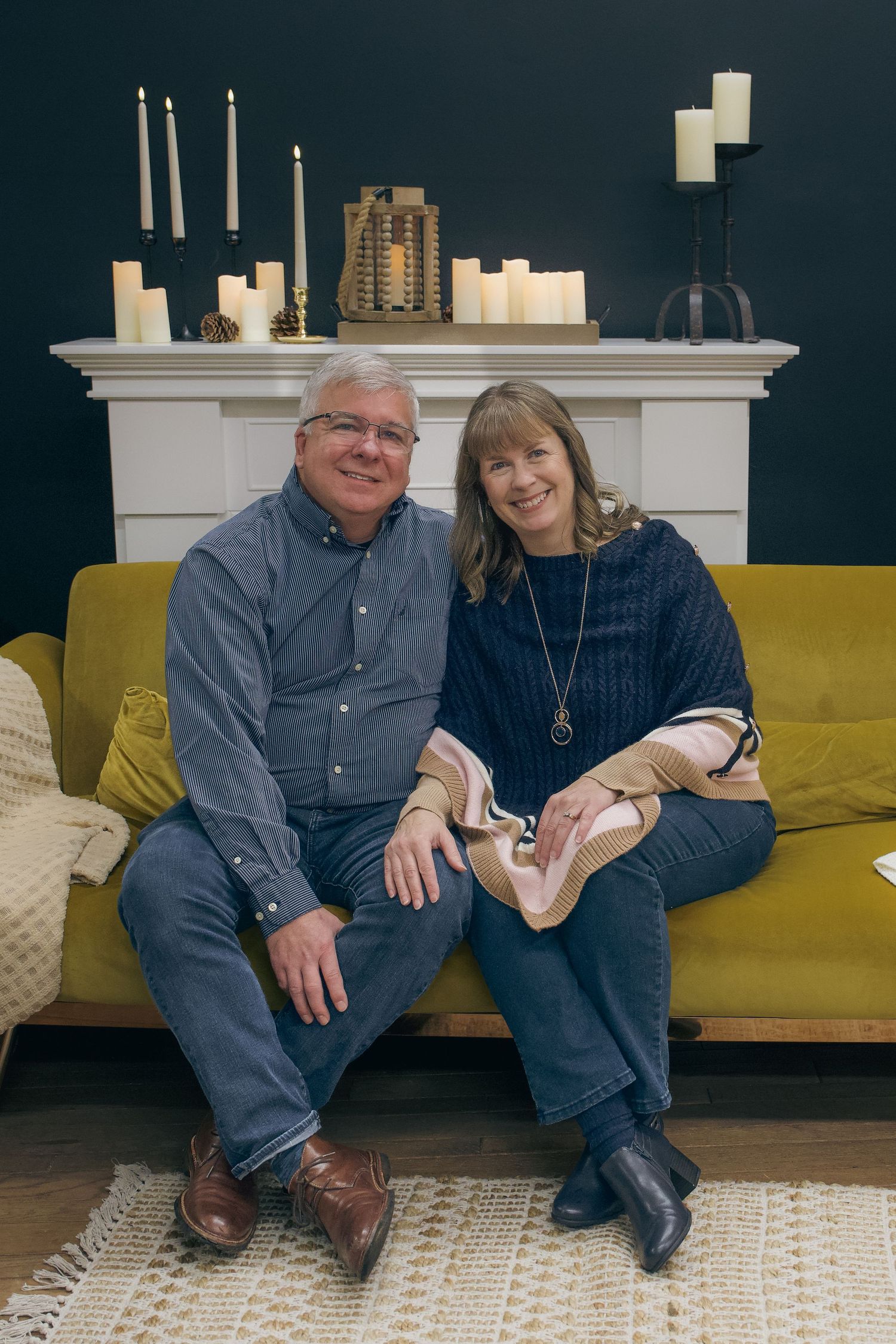 Two people sit together on a yellow couch in a room with dark walls and white trim.