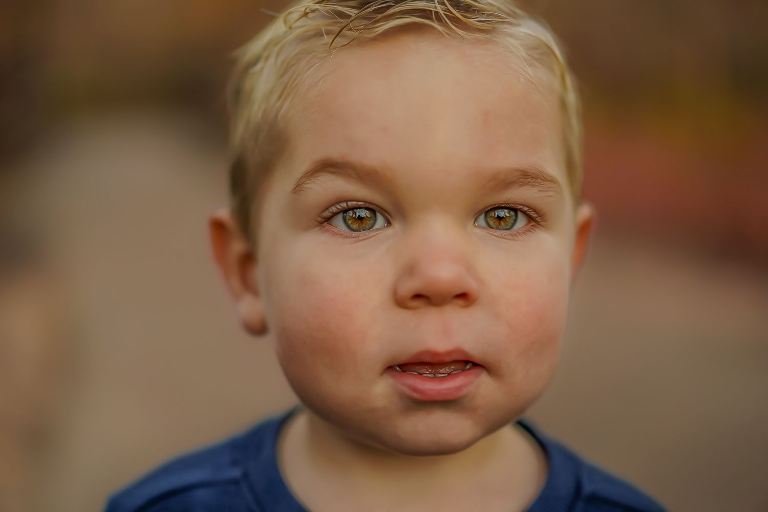 Close up portrait of a young child with blonde hair and green eyes wearing a blue shirt against a blurry background.