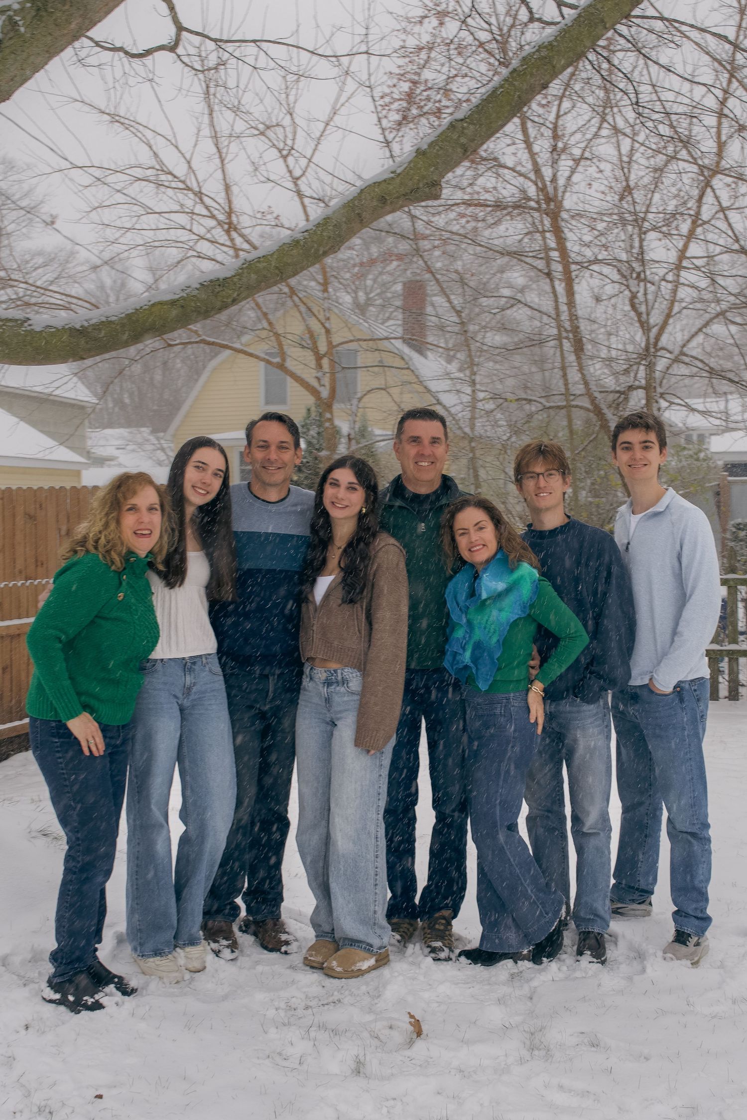 A group of people wearing casual winter clothing stand together in the snow during a snowfall.