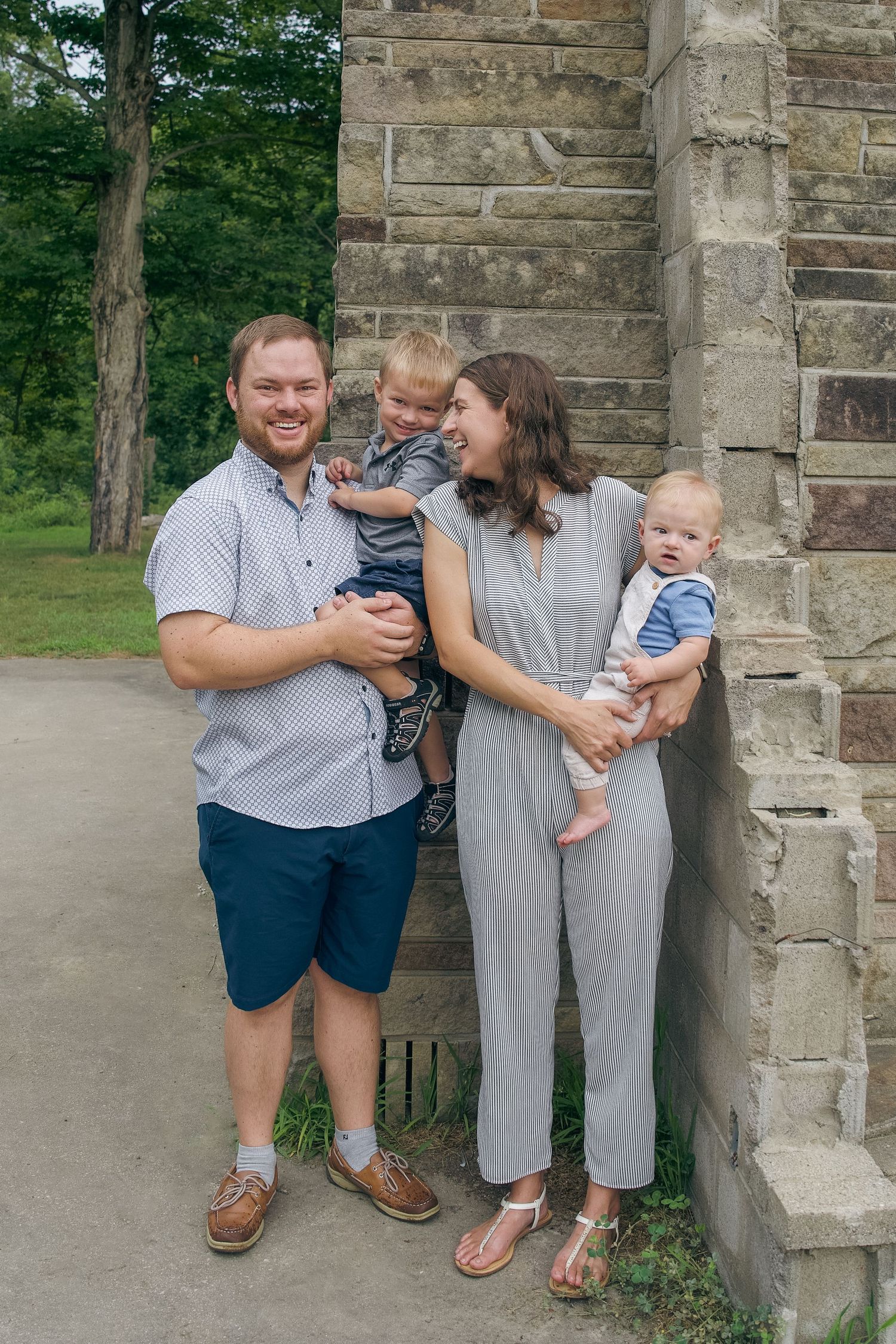 A family stands together against a stone church wall on a summer day, wearing coordinated blue and gray outfits.