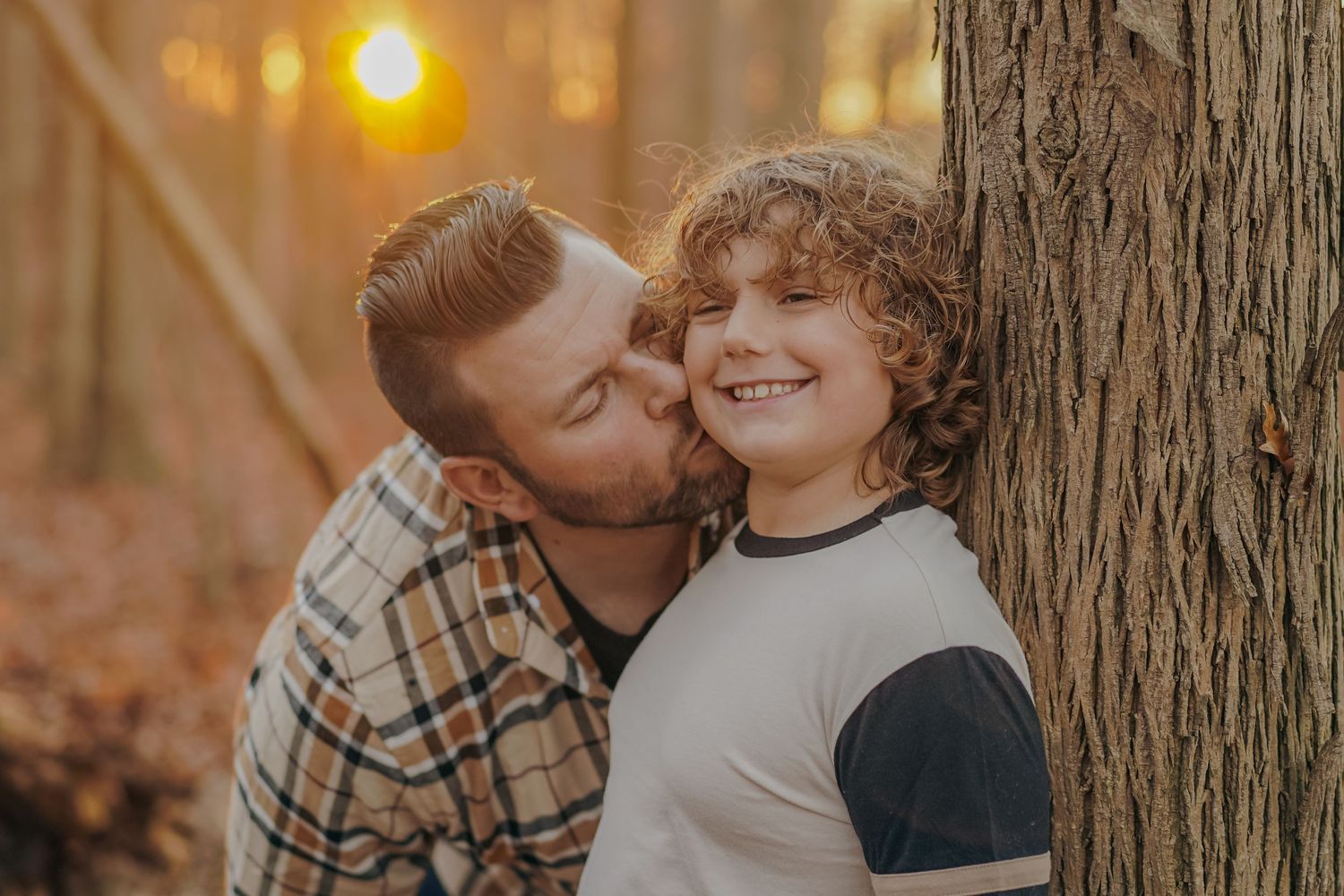 A touching autumn moment between parent and child by a tree trunk at sunset with warm golden bokeh in the background.
