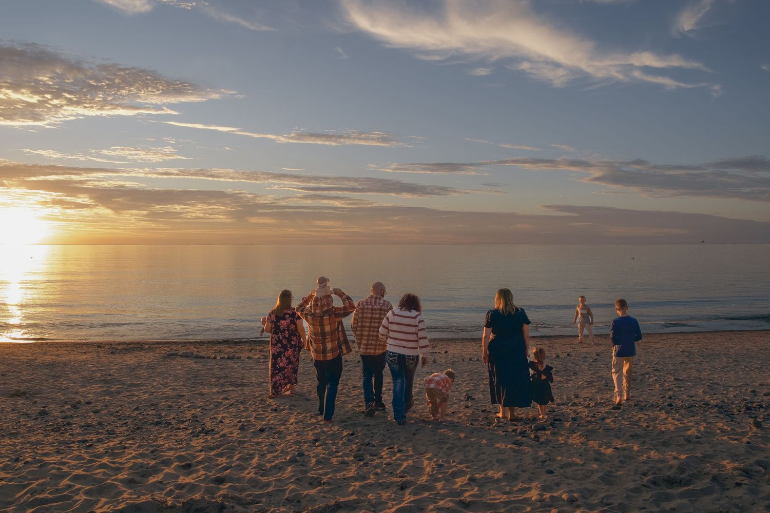 Silhouettes of people gathered on a beach watching a vibrant sunset over the ocean.