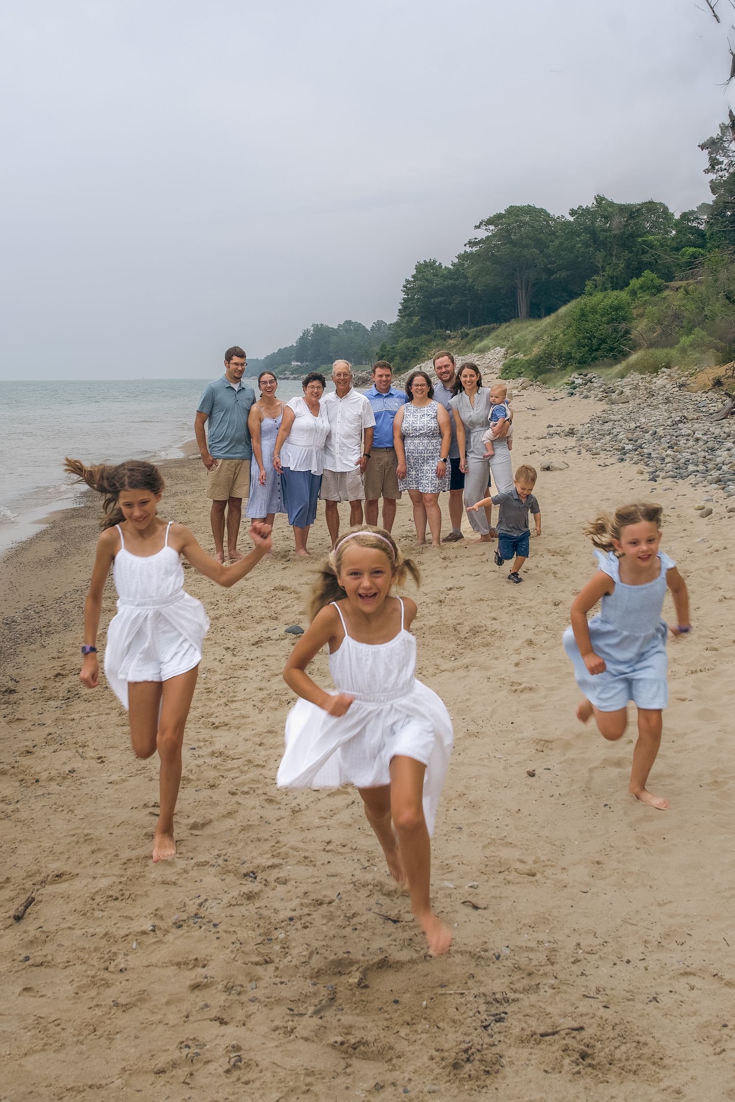 A group of people enjoying a summer day on a sandy beach with trees and cliffs in the background.