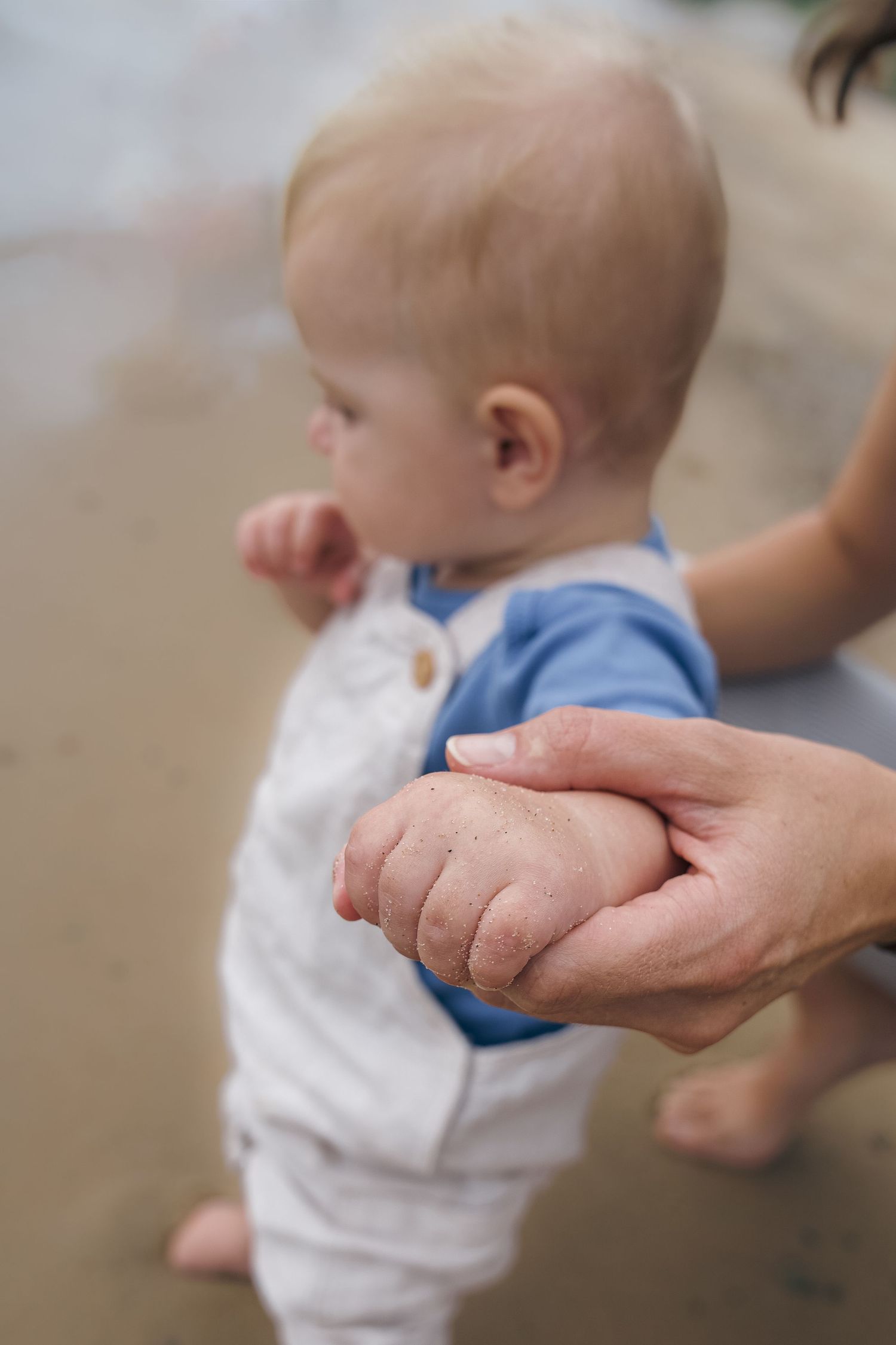 A tiny hand grasps an adult's finger while wearing a white and blue outfit.