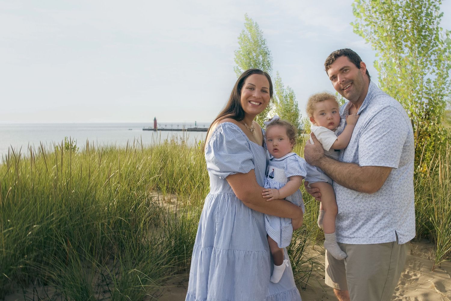A family stands together in a golden wheat field during sunset while wearing white and light colored clothing.
