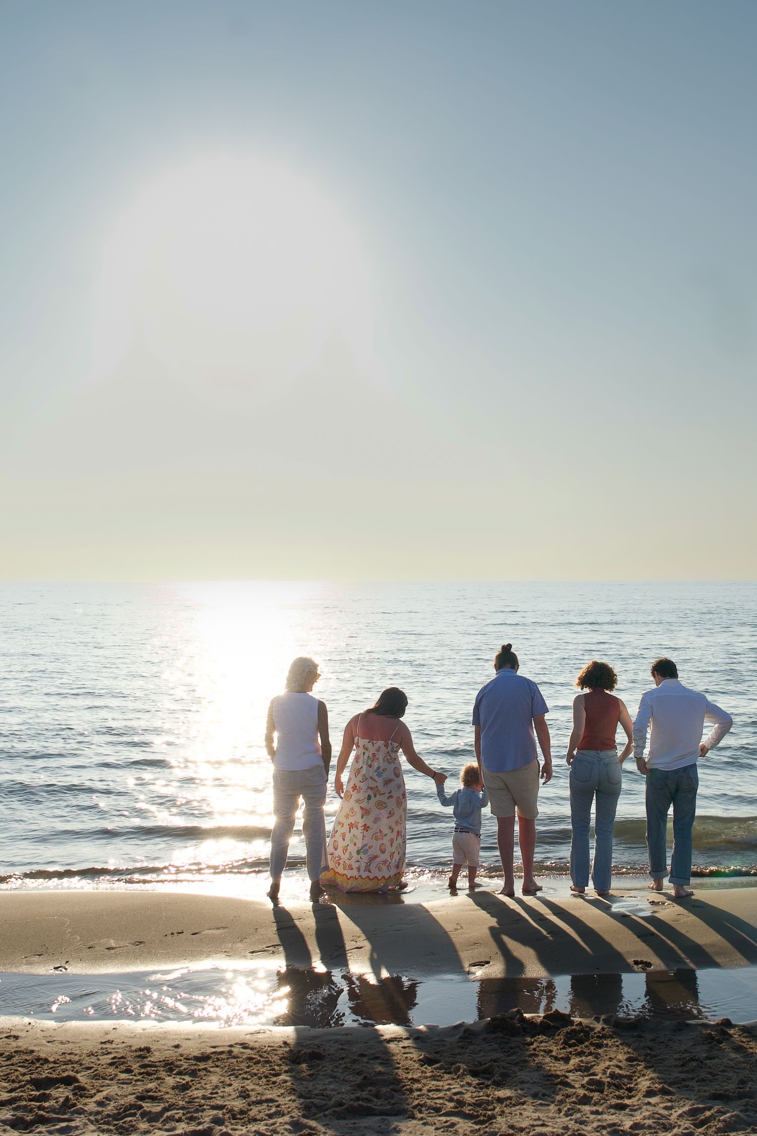 A group of people stand together on a beach at sunset, silhouetted against the golden ocean horizon.