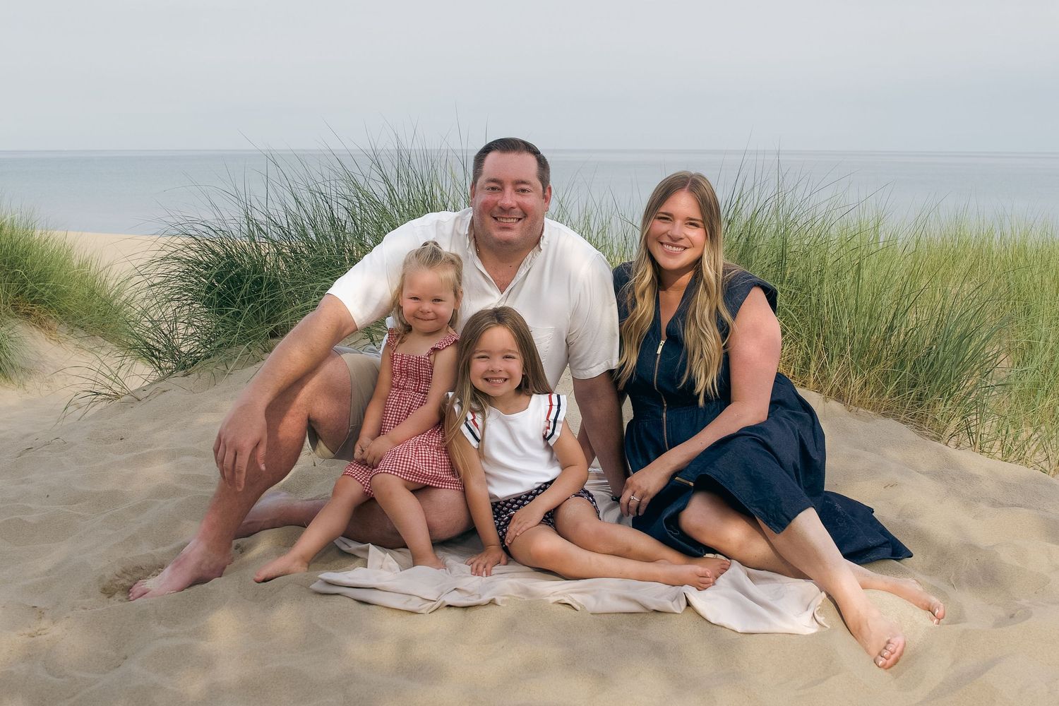 Group relaxing and posing on sand dunes at a beach during golden hour wearing white and navy blue outfits.