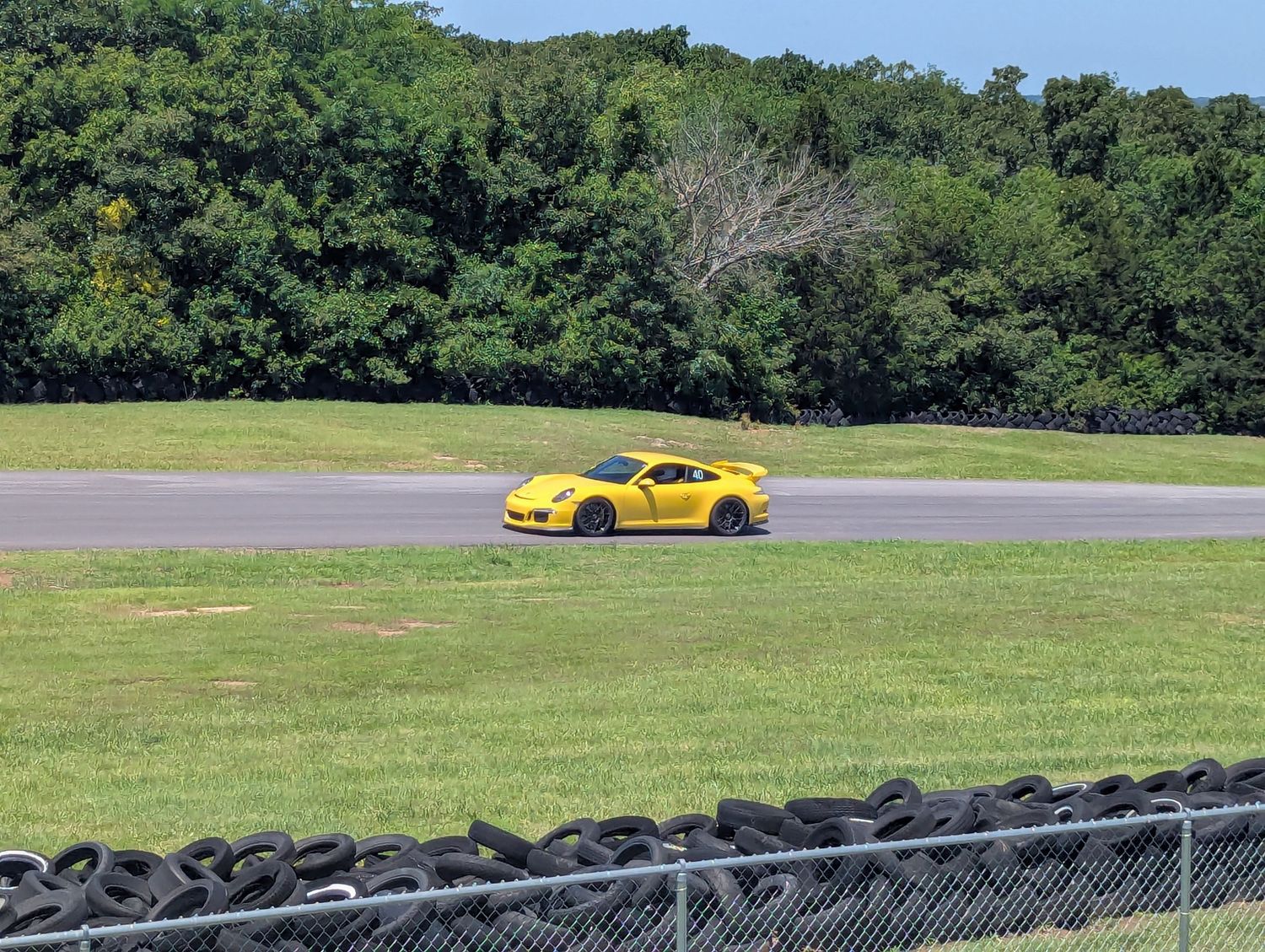 Yellow sports car racing around a curve on a track lined with tire barriers and trees.