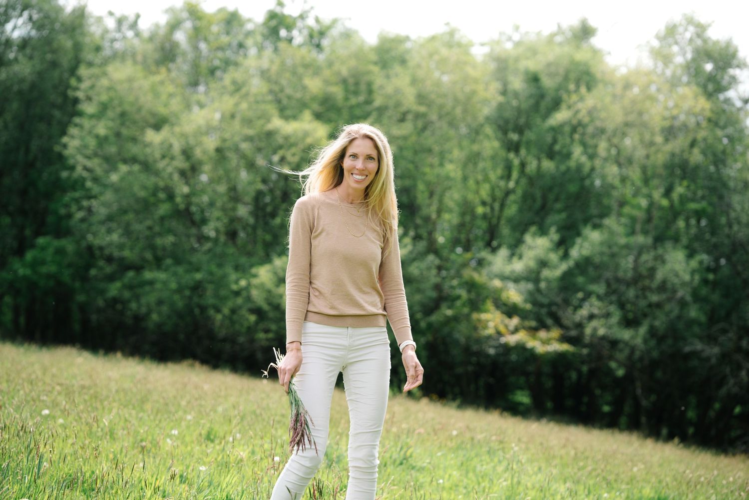Woman in yellow top and jeans stands thoughtfully on empty beach.