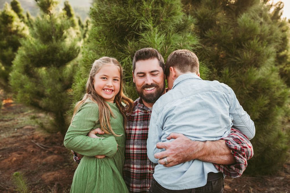 People embrace while posing for candid photos in a pine forest setting.