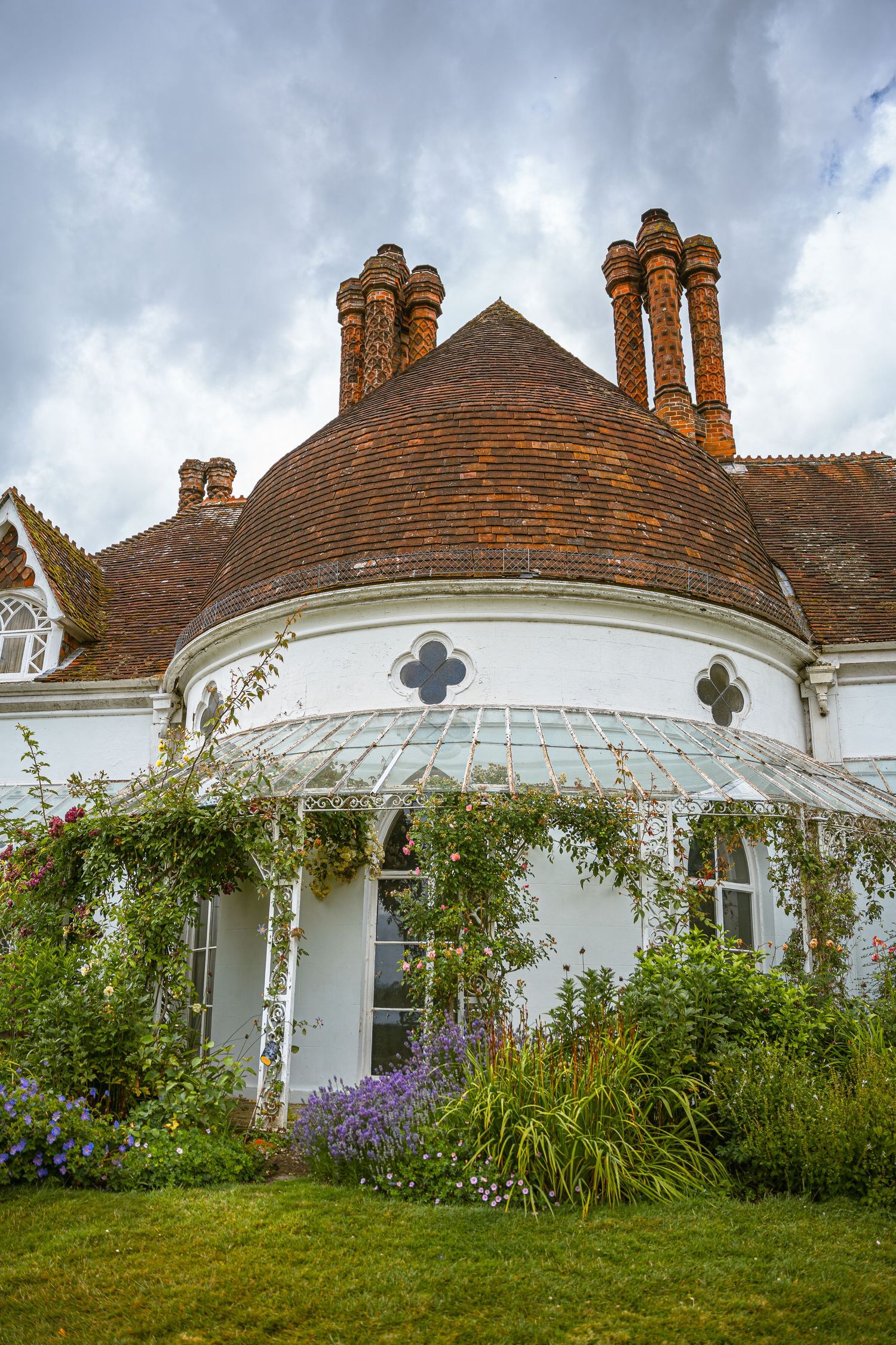 Beautiful Victorian cottage with ornate chimneys, white walls, arched conservatory and flowering garden border in England.