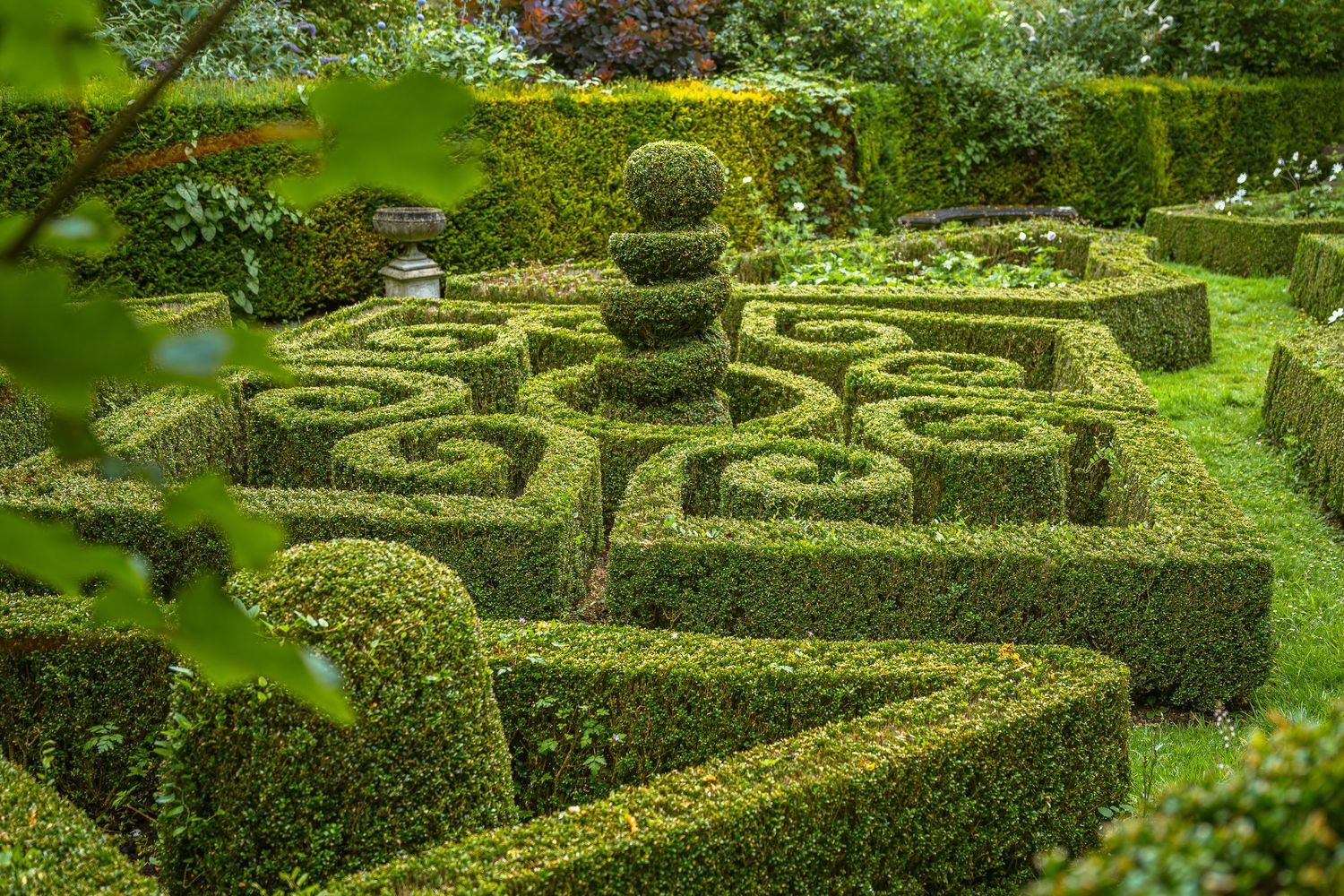 Ornate topiary garden features intricate geometric patterns with manicured hedges shaped into spirals and curves.