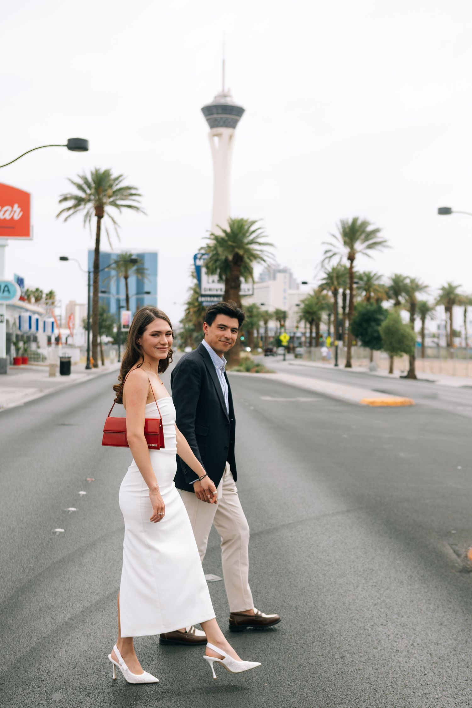 Couple in formal wear walking along Las Vegas street with Stratosphere tower in background.