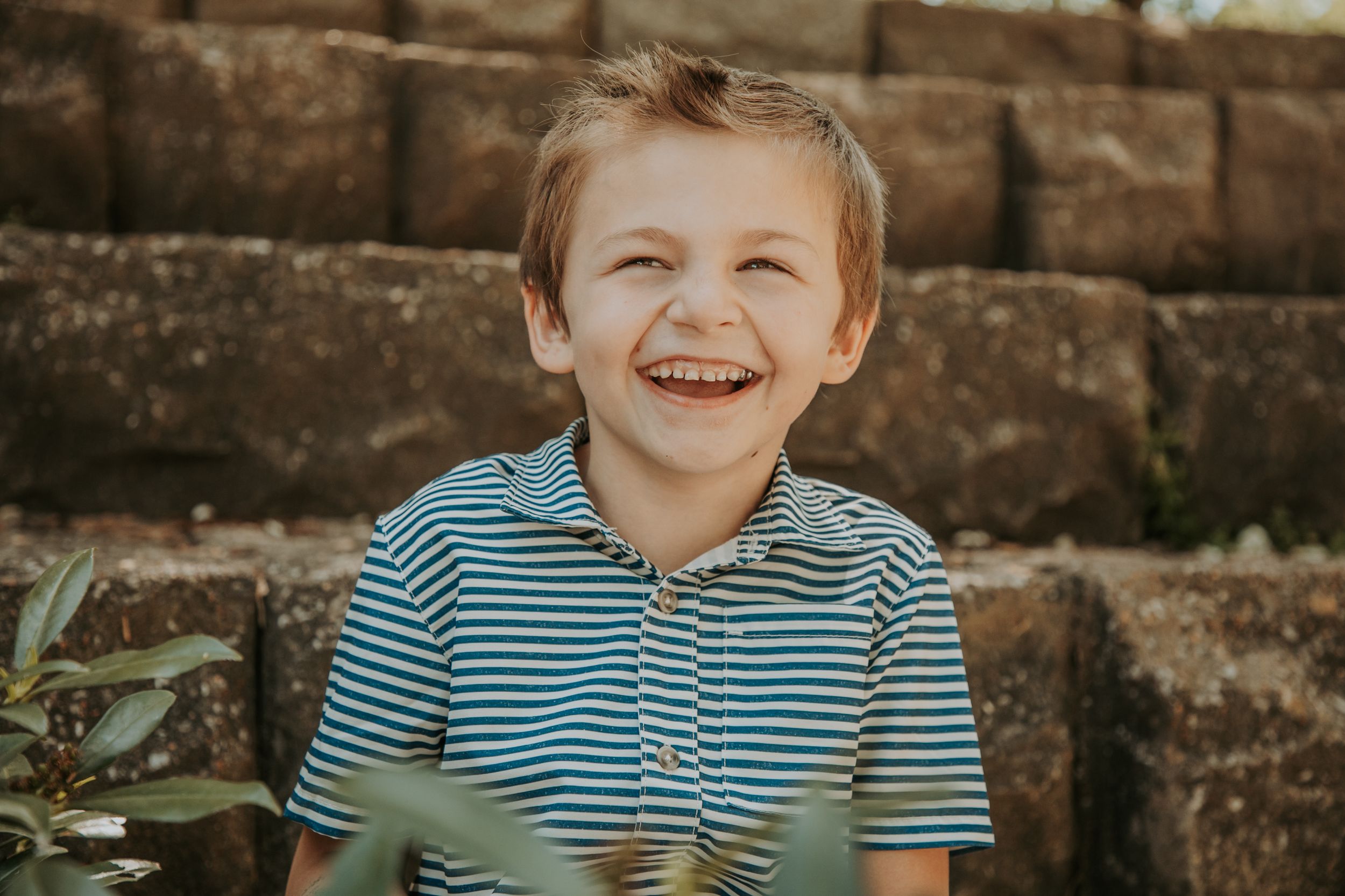 Close up of child with bright smile wearing striped shirt against stone wall background.