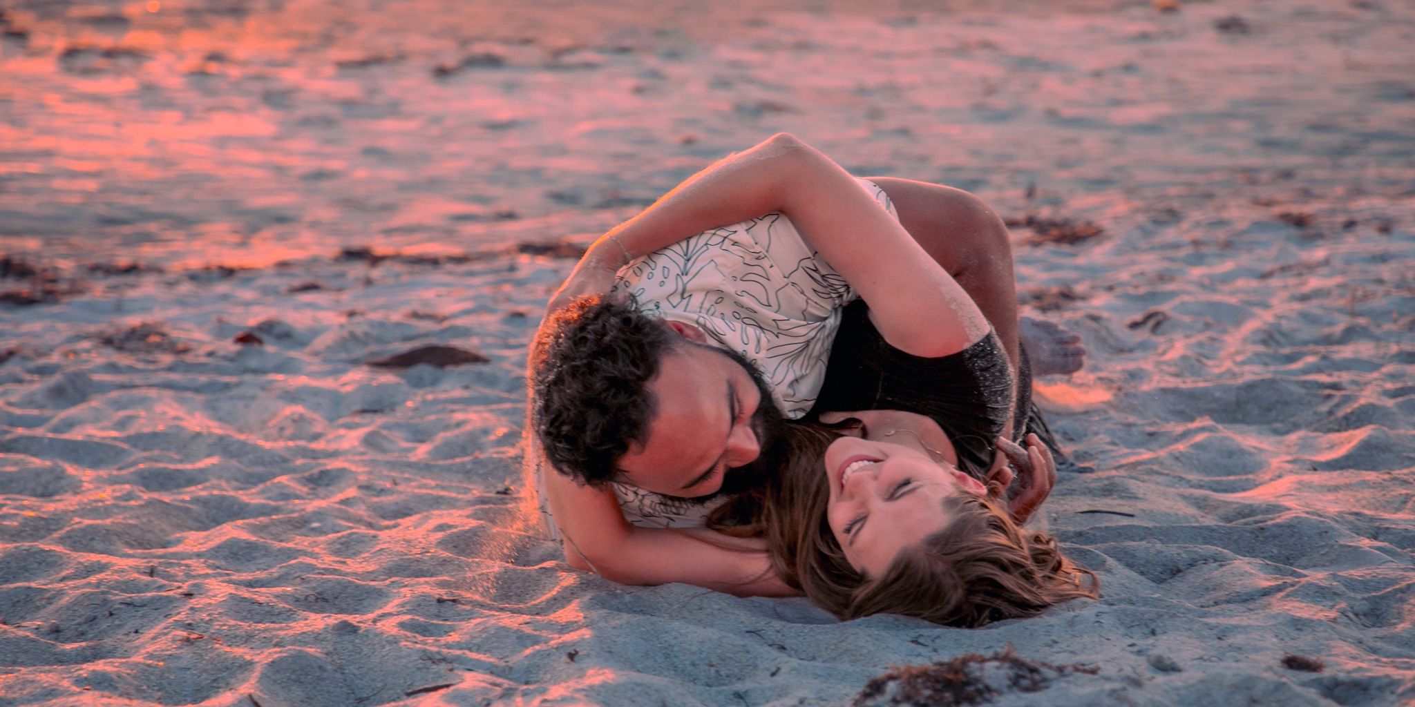 A couple embraces on sandy beach during sunset creating romantic silhouette.