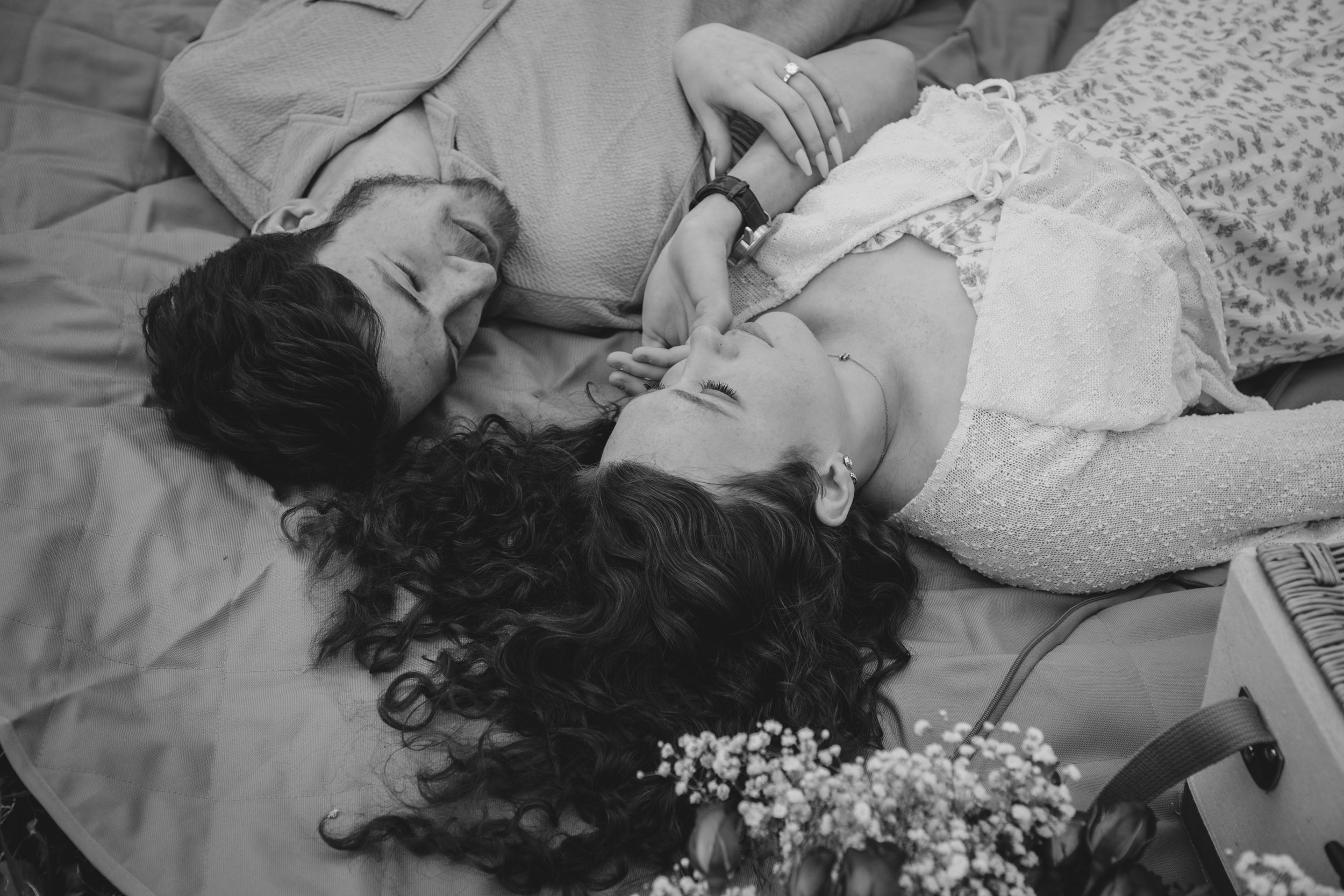 An intimate black and white portrait of a couple lying down with flowers.