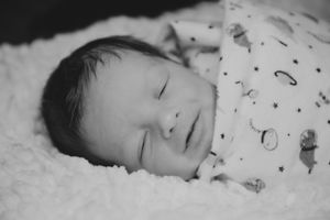 A sleeping newborn baby in black and white wearing patterned sleepwear on soft blanket.
