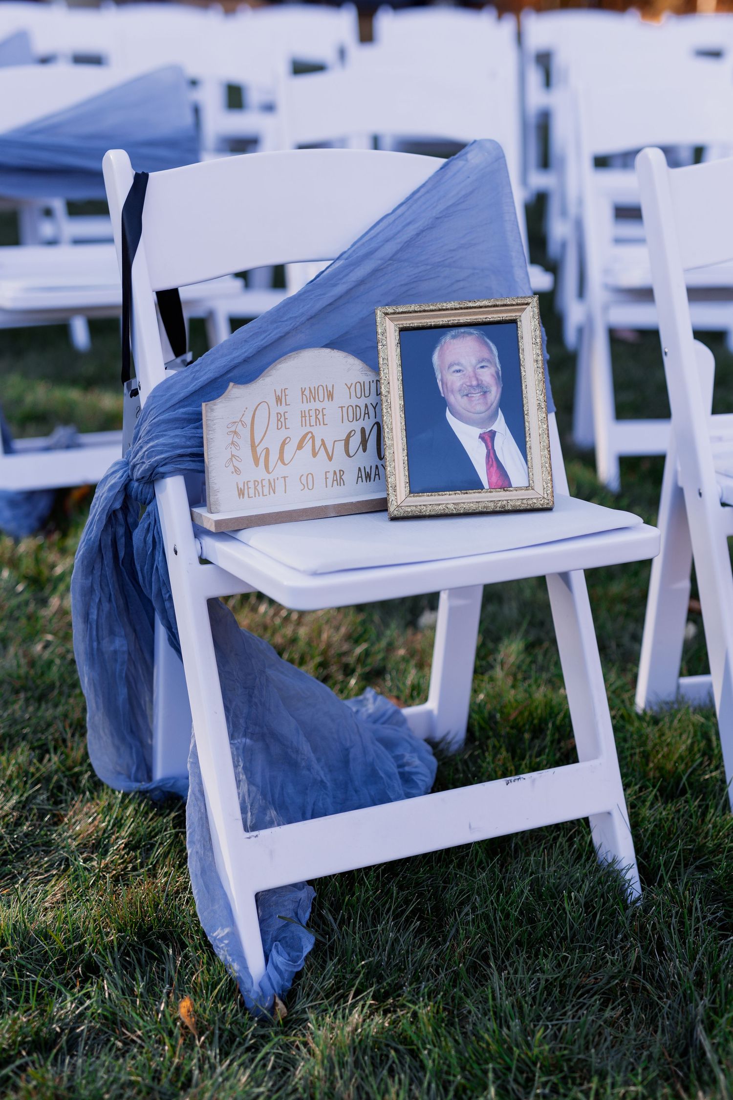 A white folding chair with framed portraits and a blue fabric draped over it at an outdoor event.