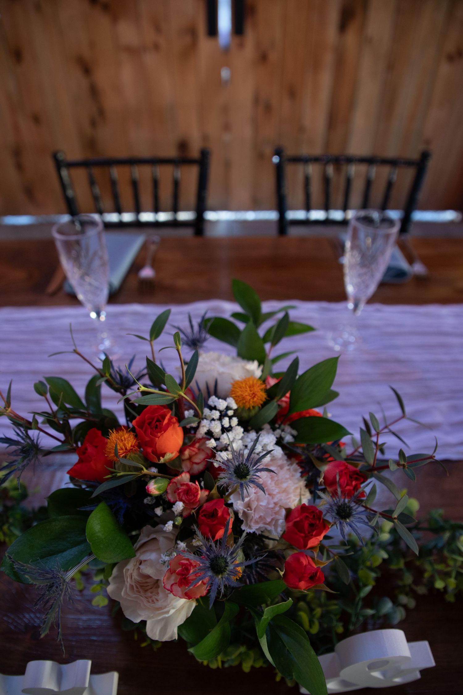 Elegant floral centerpiece with red and orange blooms on a table set with crystal glasses.