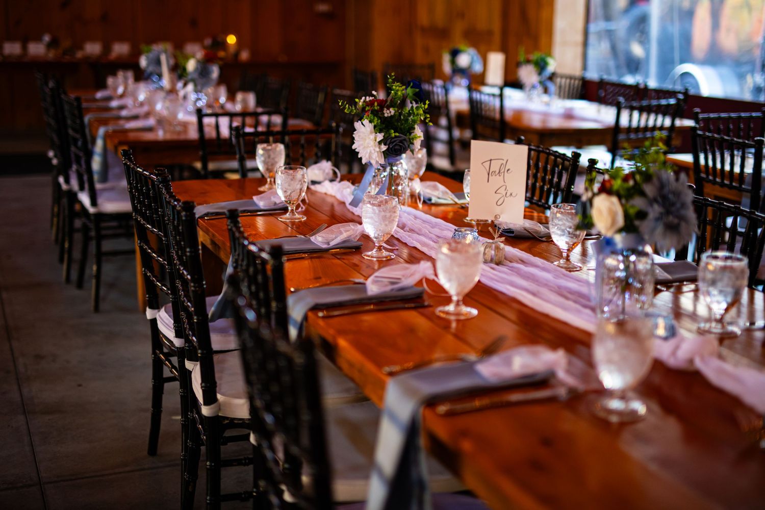 Long wooden tables set for a wedding reception with black chairs and elegant place settings.