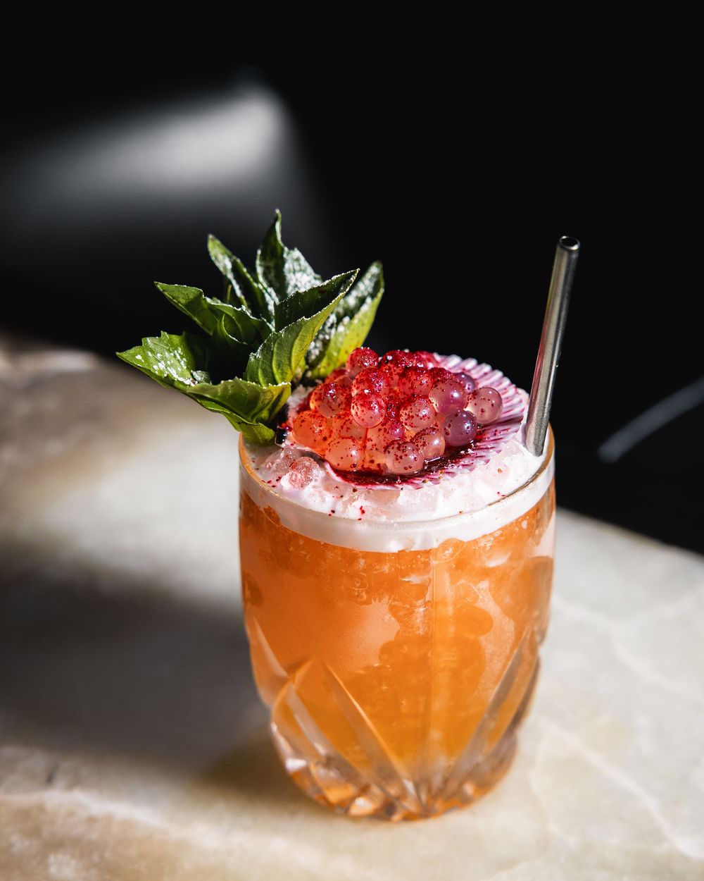 Orange cocktail with fresh strawberry and mint garnish in a crystal glass.