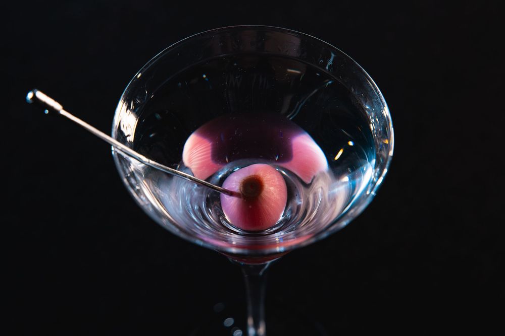 Sophisticated martini glass with red cherry garnish in moody dark lighting.