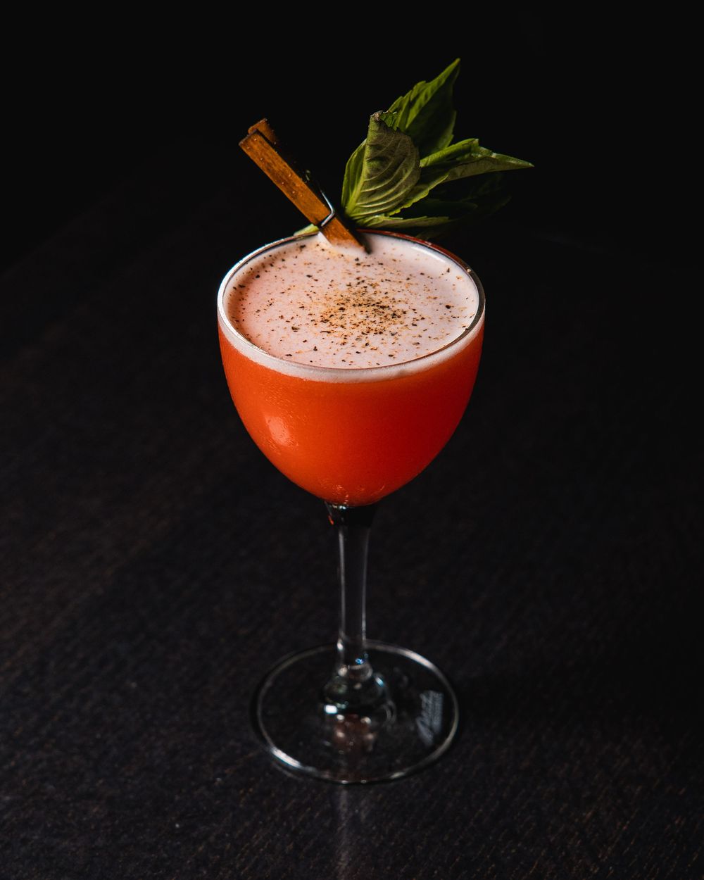 Pink cocktail with mint garnish in coupe glass against dark background.