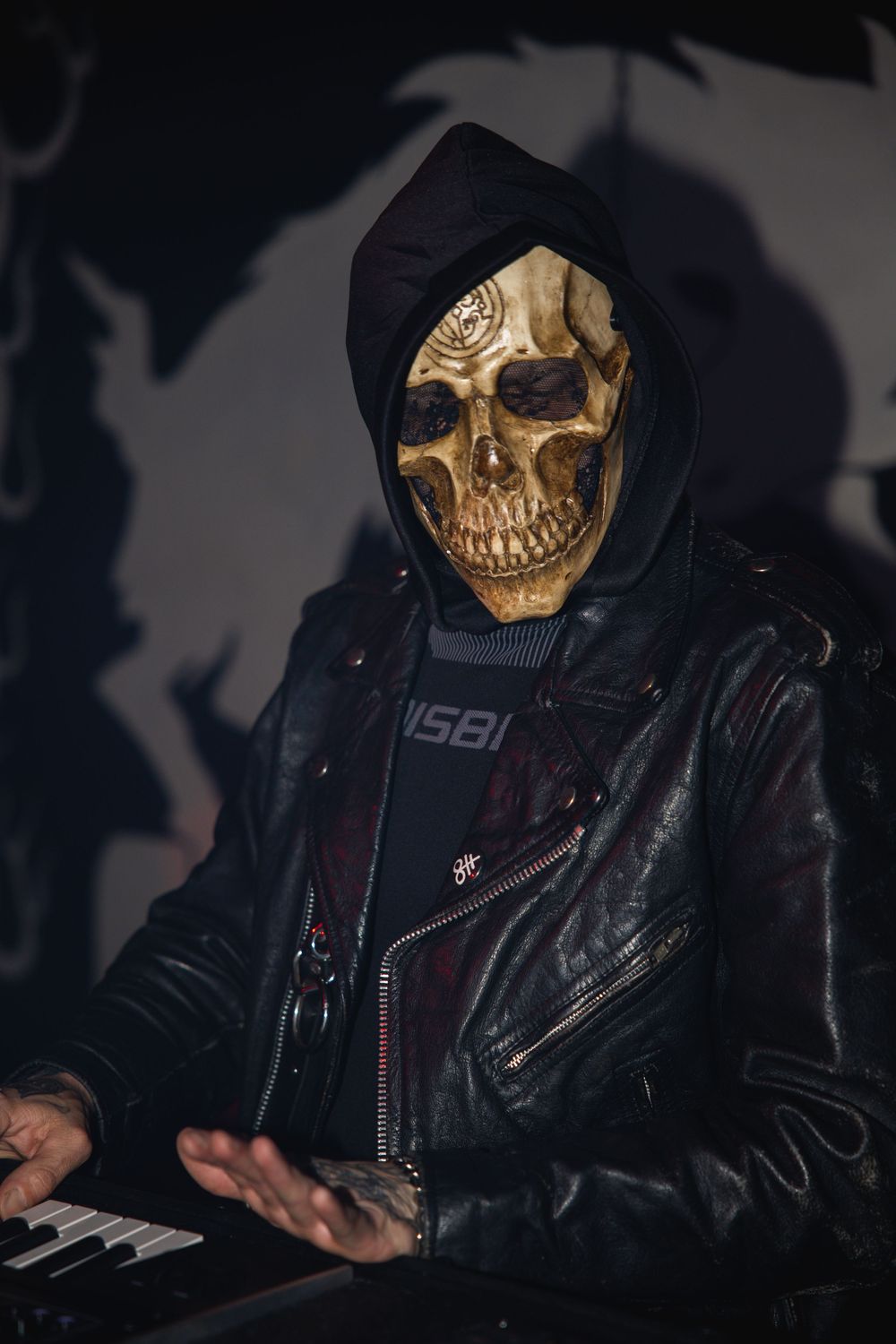 Person wearing a dramatic gold skull mask and black leather jacket in dark atmospheric lighting.