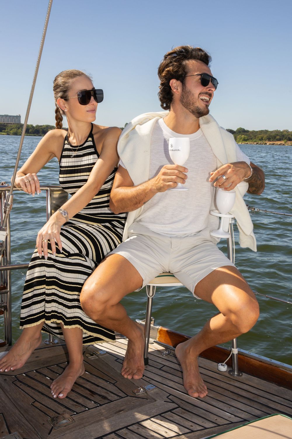 Couple relaxing on wooden dock by lake enjoying drinks on sunny summer day.