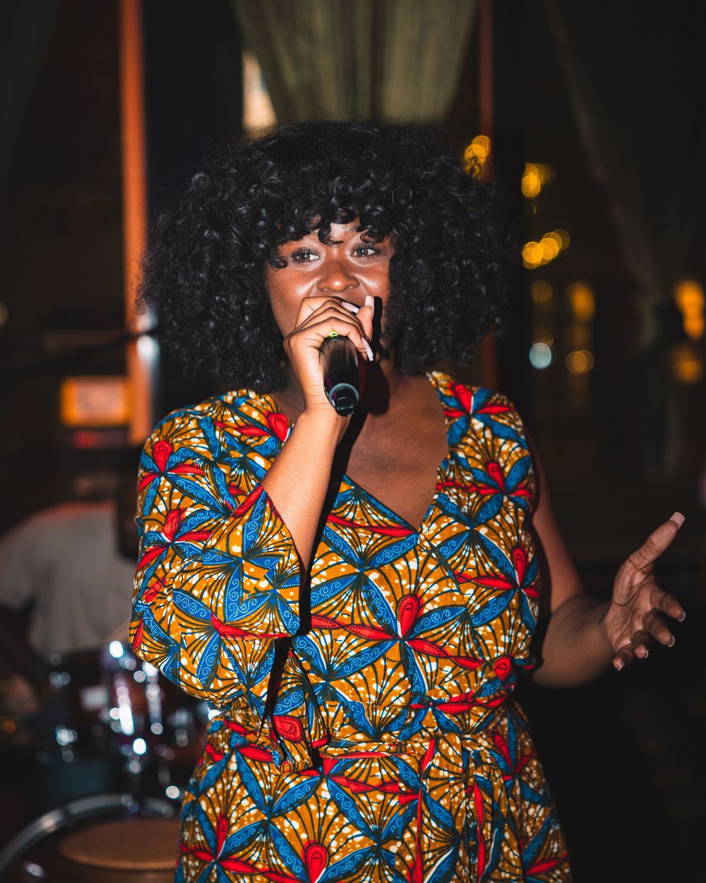 Singer performing on stage wearing vibrant patterned clothing in colorful lighting.