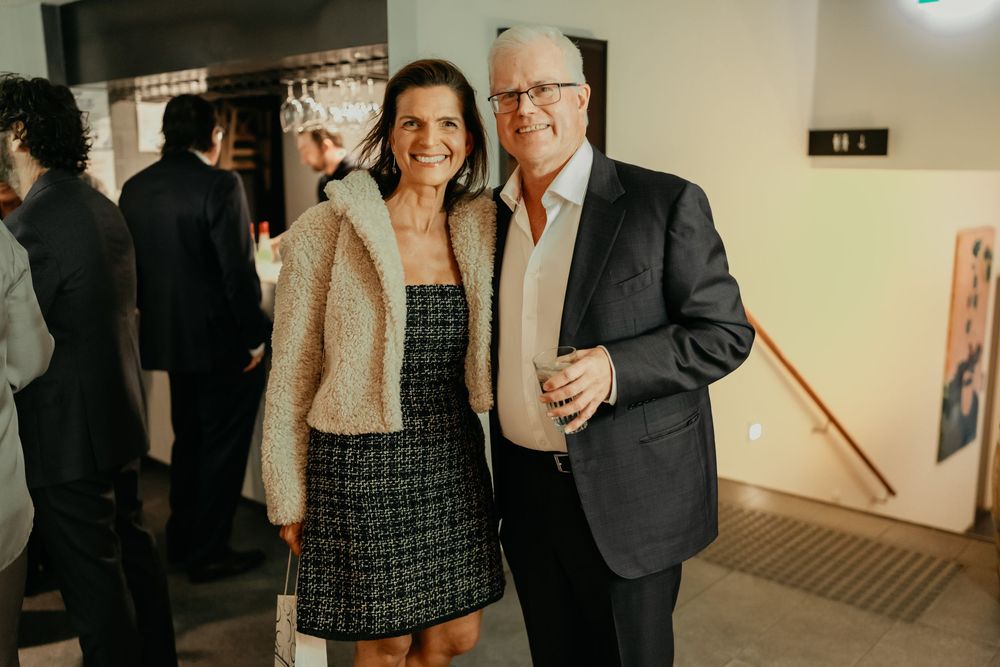 Guests mingle at a gallery opening event, with artwork displayed on white walls in the background.