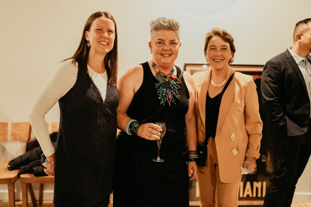 A group of people gathered for an indoor event smile and socialize while holding drinks and refreshments.