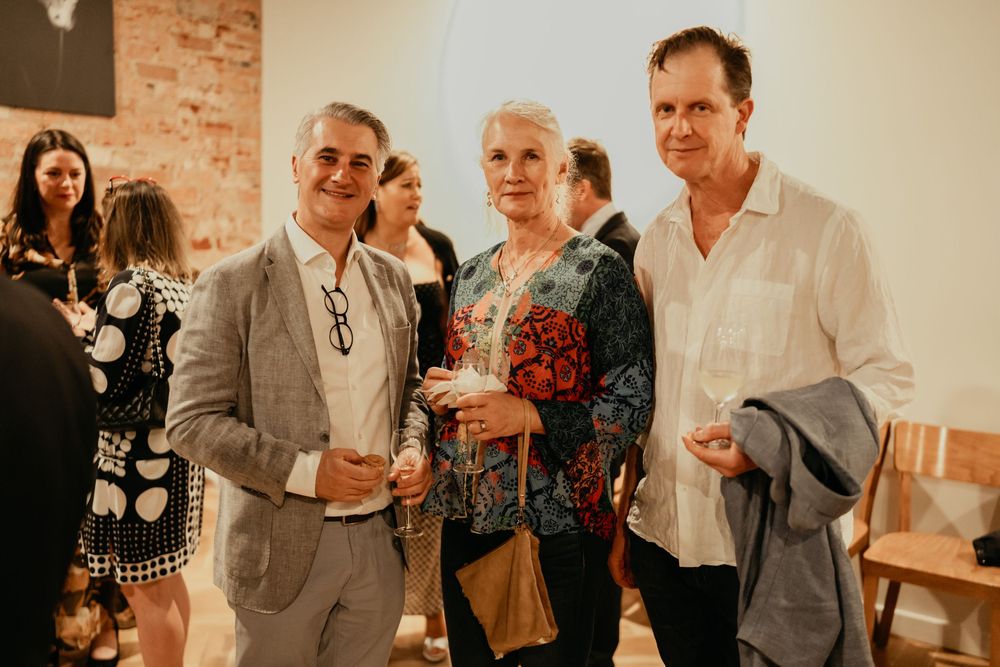 Group of people socializing and mingling at a casual indoor gathering with exposed brick wall in background.