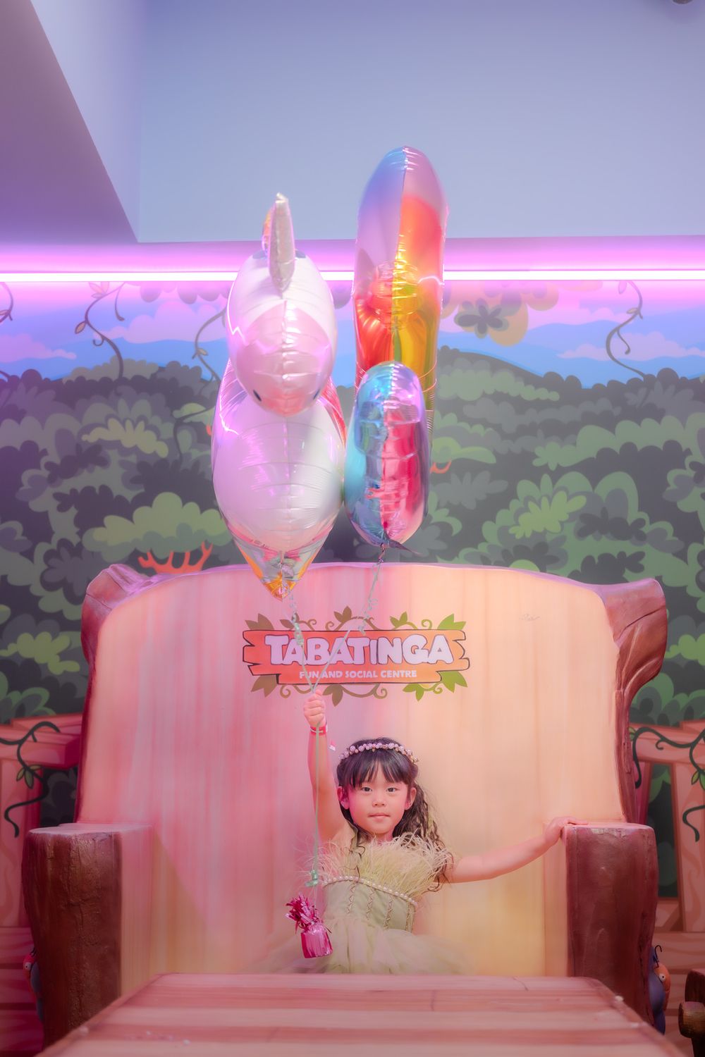 Decorative display featuring pink chairs and balloon decorations with a Tapatinga theme against a painted wall backdrop.